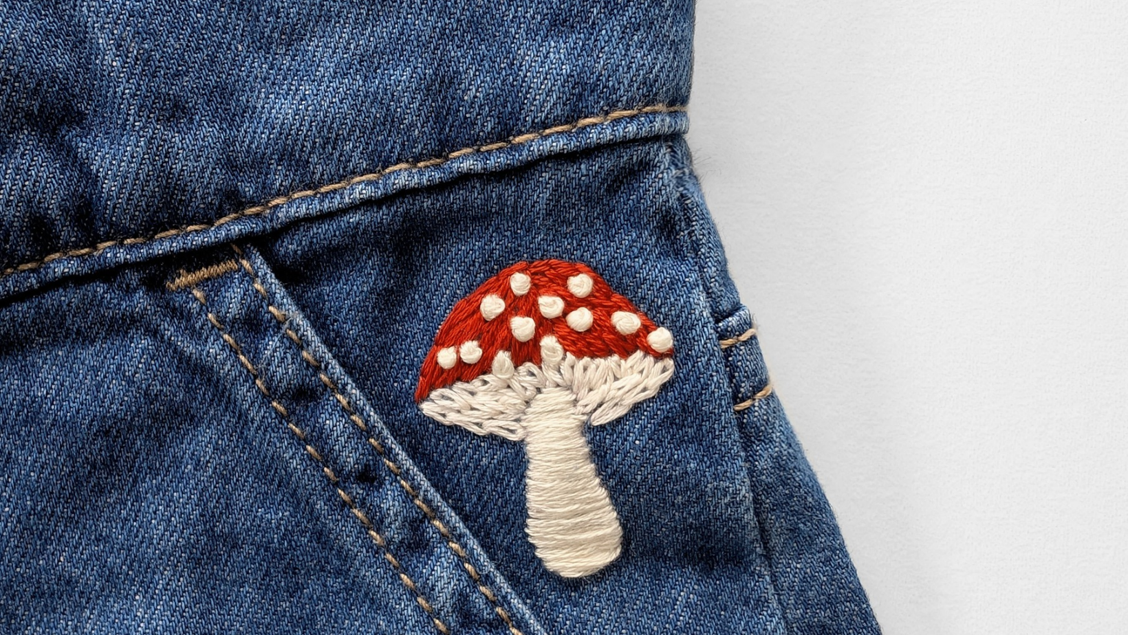 A red and cream toadstool embroidered on the pocket of blue denim jeans.