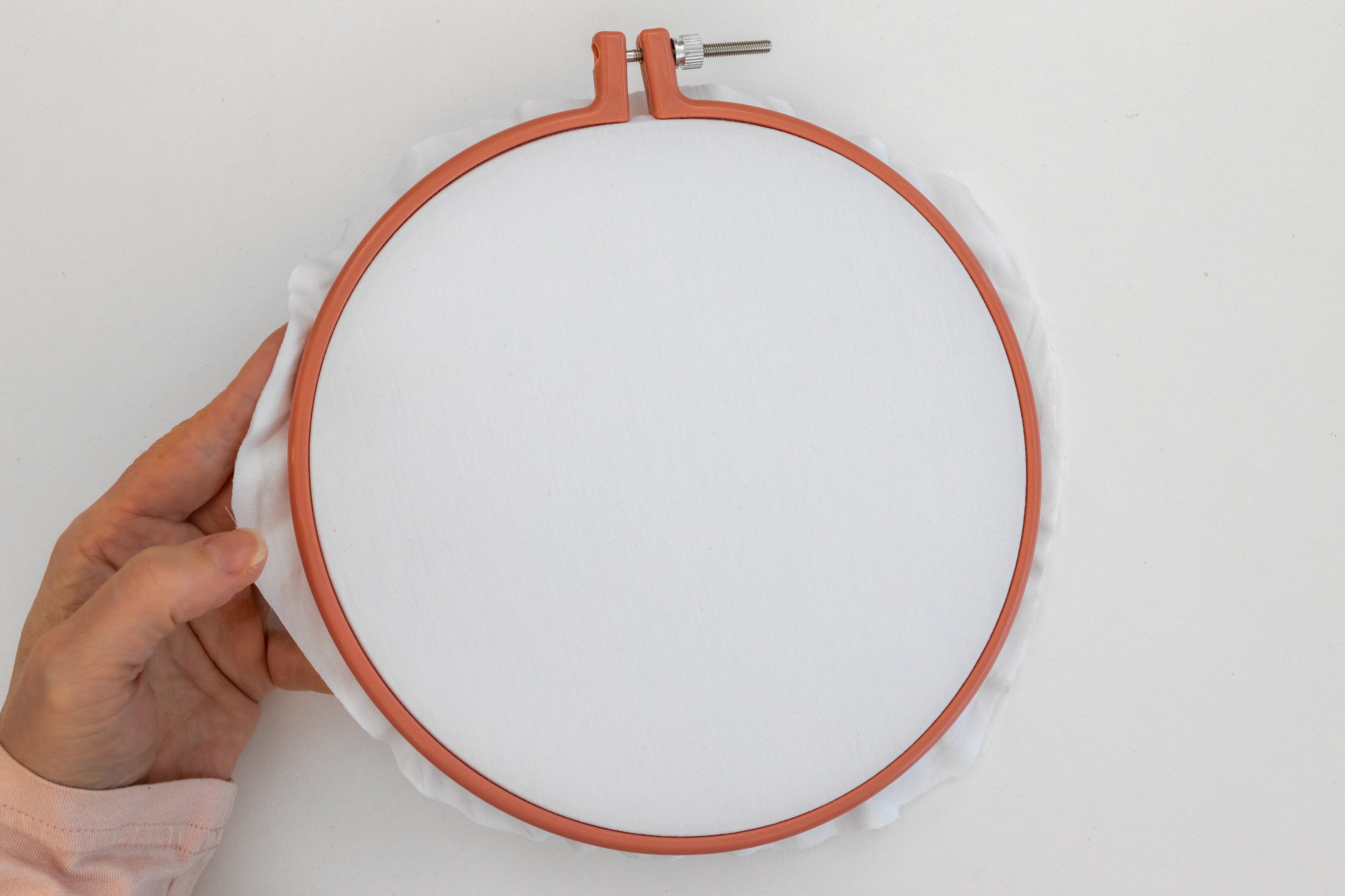 A hand holds a hoop with tightened fabric in it.