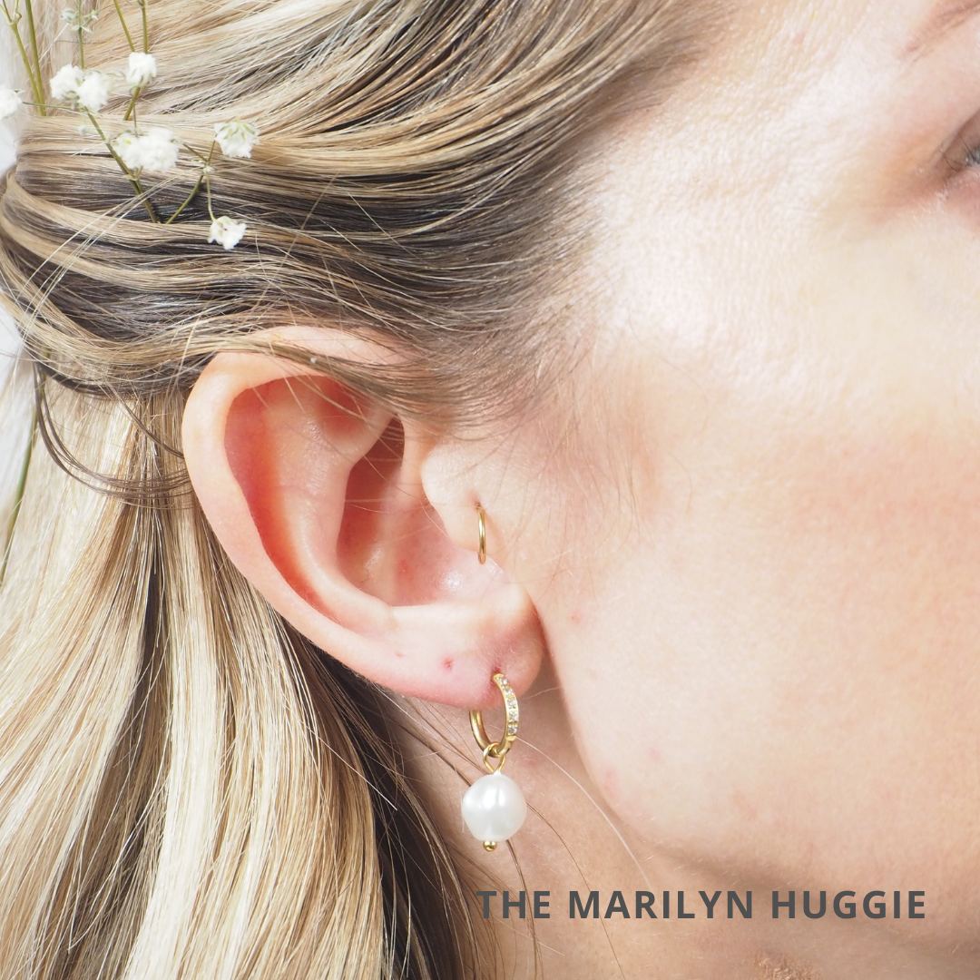 Close-up of a woman's ear with a gold hoop with a pearl charm drop.