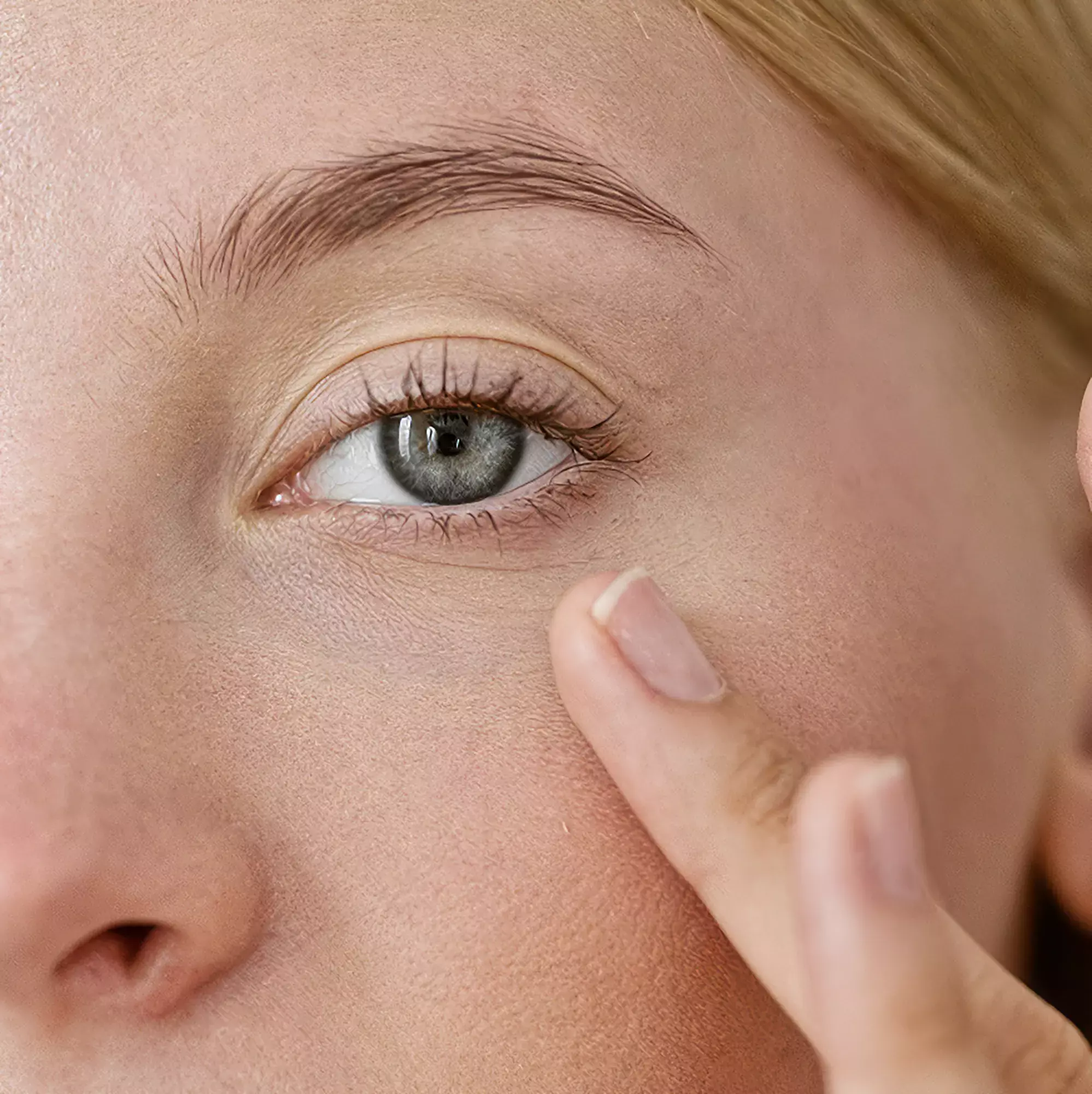 A woman gently touching her under-eye area.