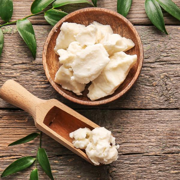 wooden background. shea butter in a wooden bowl and a wooden spoon surrounded by green leaves.