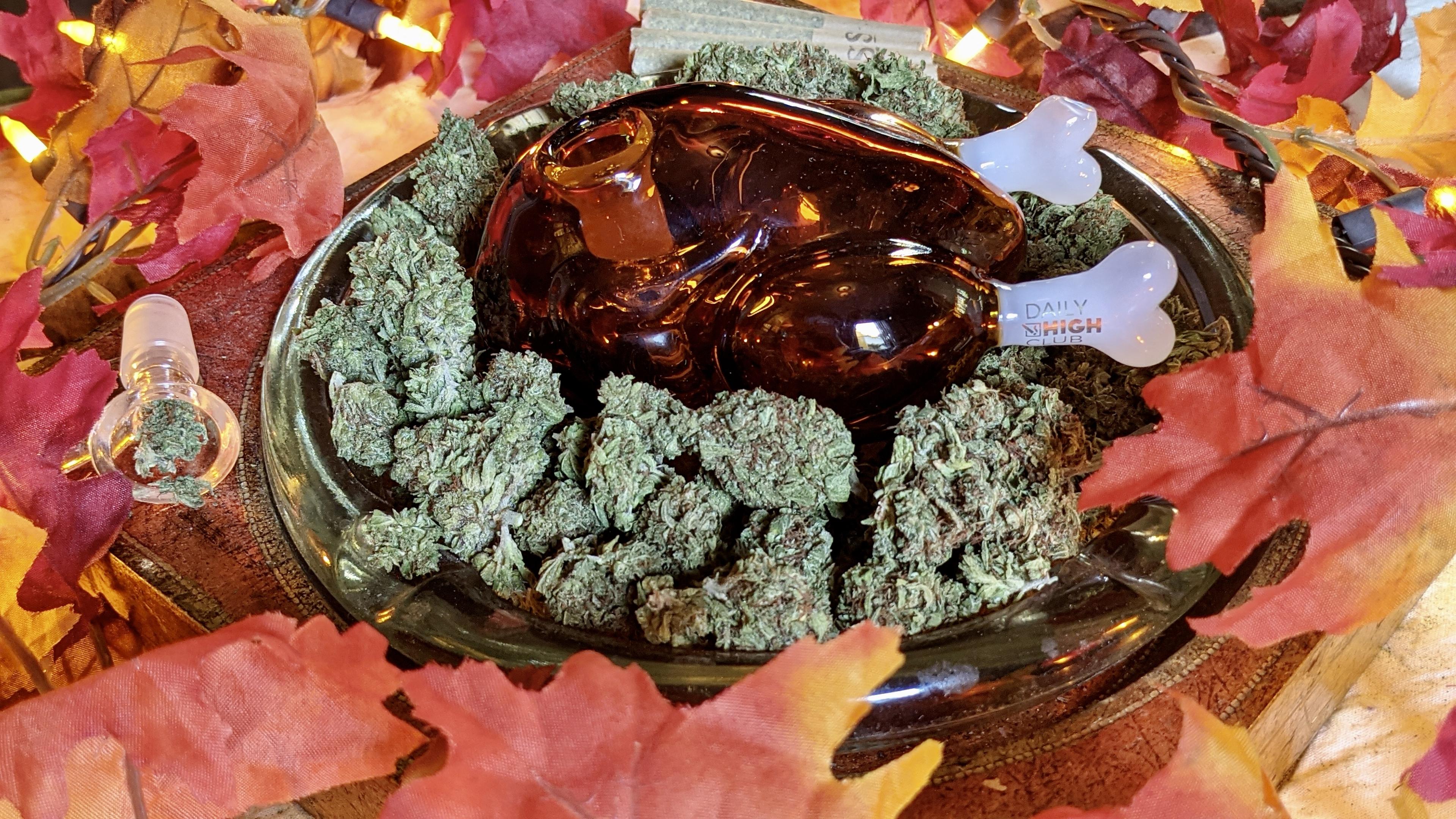 A comedic, turkey-shaped dry handpipe surrounded by autumnal leaves and a golden ashtray, showcasing alternative flower consumption for a festive Danksgiving menu alongside edible Thanksgiving recipes.