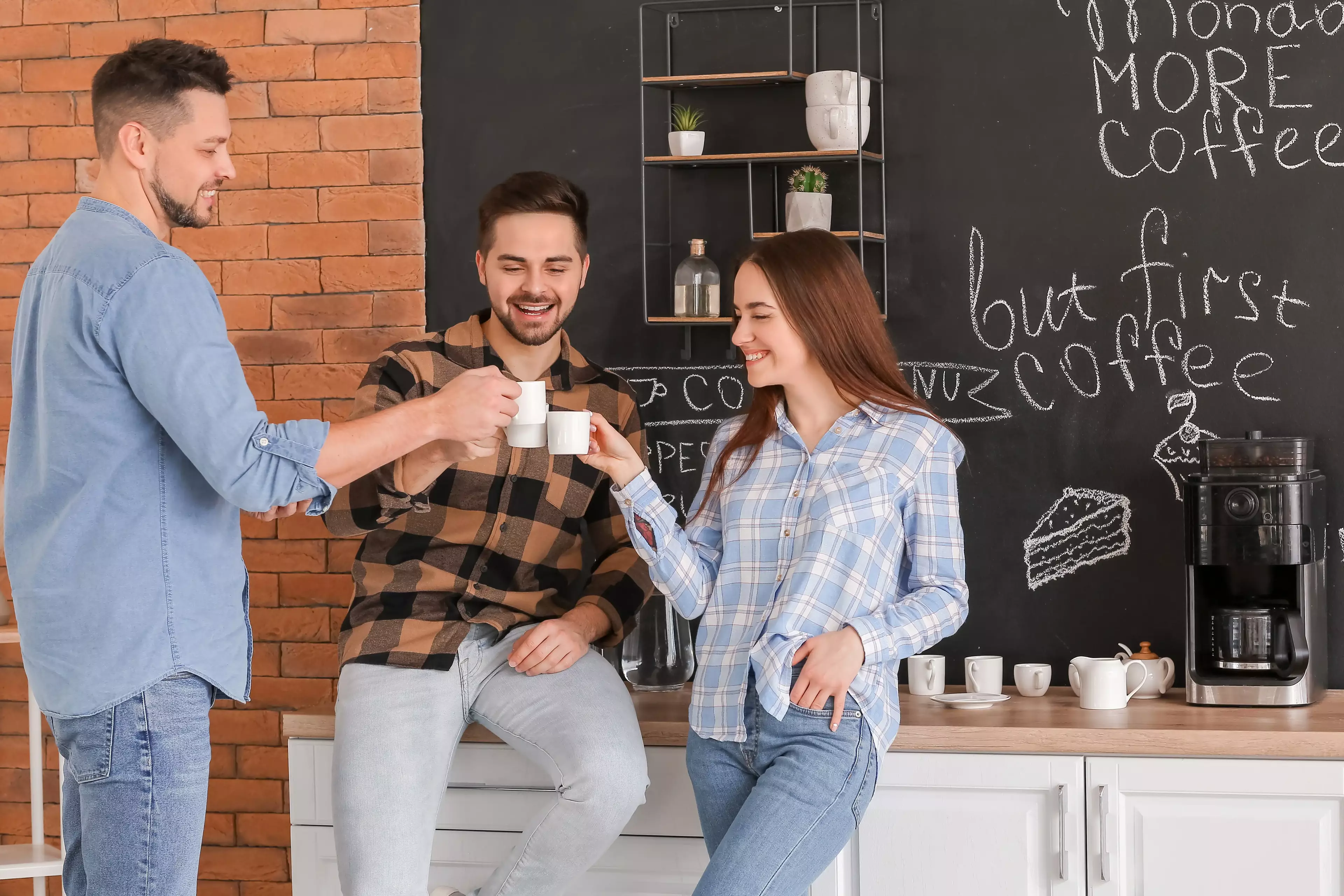 Group of friends smiling and enjoying coffee together in a modern kitchen setting.