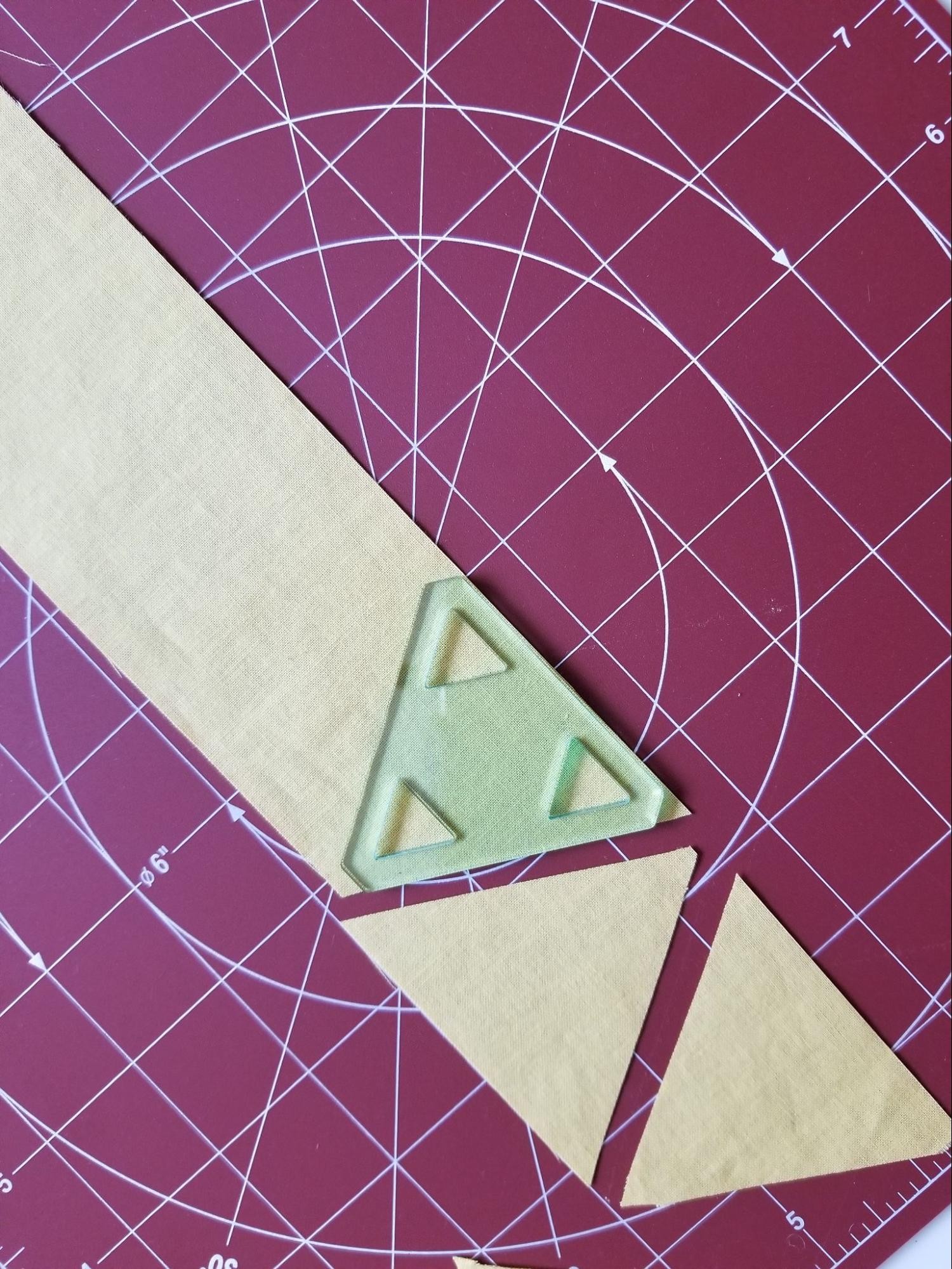 Showing two triangles cut from a strip of fabric while using a 60 degree triangle quilt template.