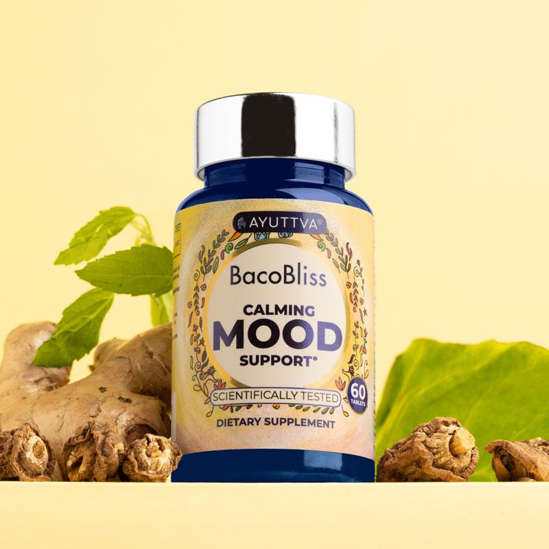 Bottle of BacoBliss Calming Mood Support dietary supplement placed alongside ginger roots, holy basil and spinach on a yellow background.