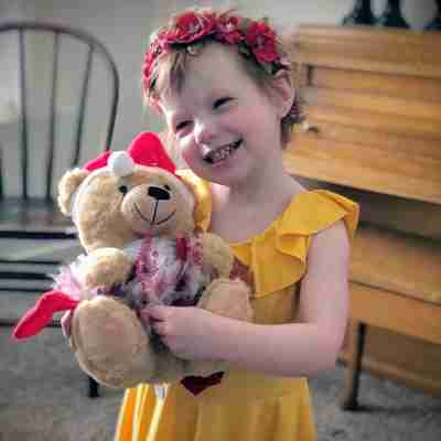 A little girl with a flower crown smiling holding a festive Christmas bear