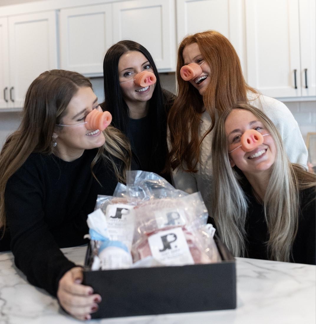four ladies with pig masks on smiling around a pork bundle box