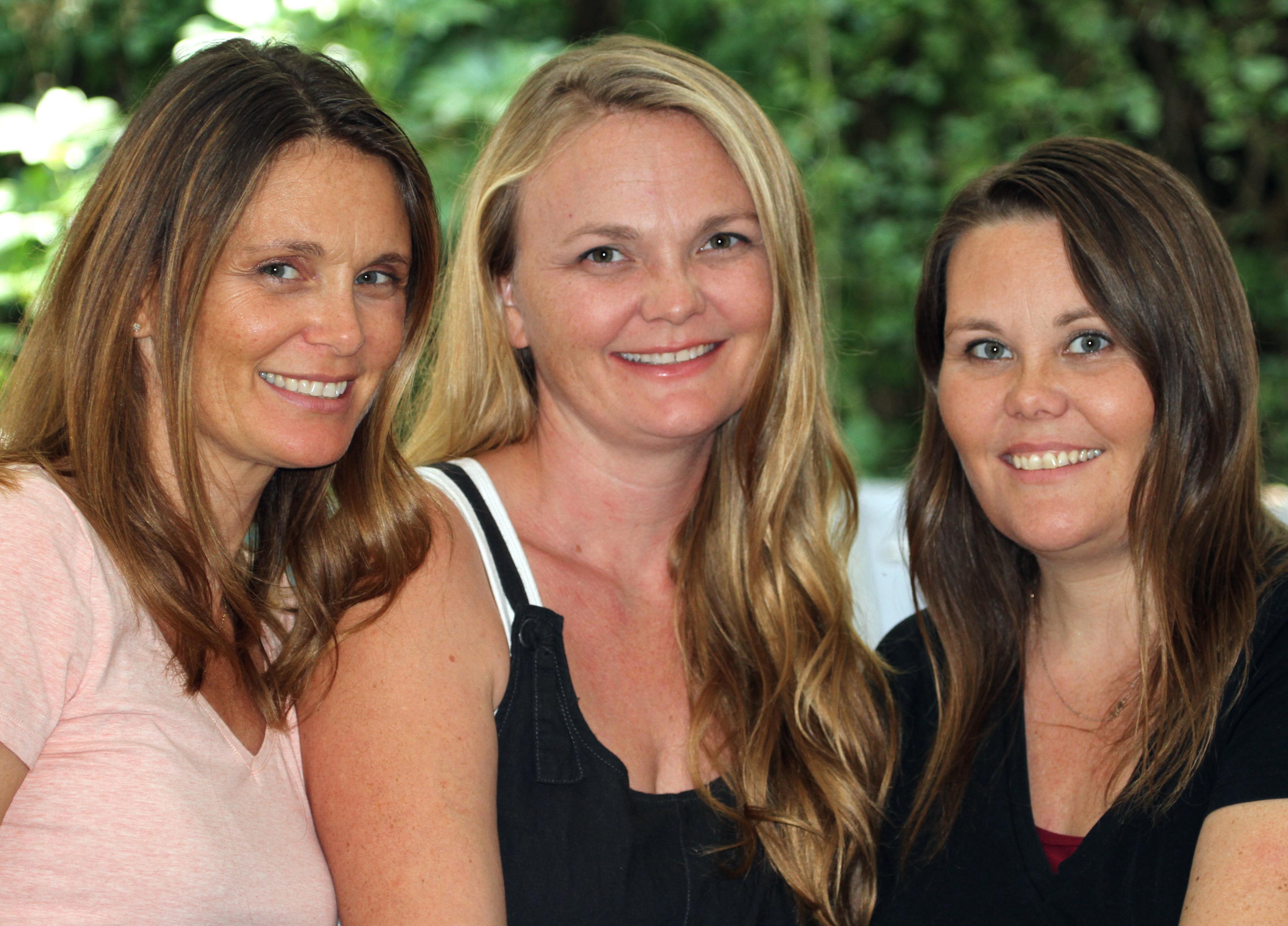 Picture of Herbal Roots founders . Jennifer, left side of image of a smiling woman with fair skin, dark and light brown hair, while wearing a light pink shirt. Emily, positioned in the middle of Jennifer and Heather , is an image of a woman with fair skin and light blonde wavy hair and smiling while wearing a black tank top. Heather, standing next to Emily positioned on the right side of the image, is a woman with fair skin, dark brown hair and smiling and is wearing a black blouse.