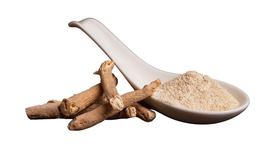 Light brown colored Ashwagandha root in a small pile next to a spoon with ashwagandha powder in it on a white background .