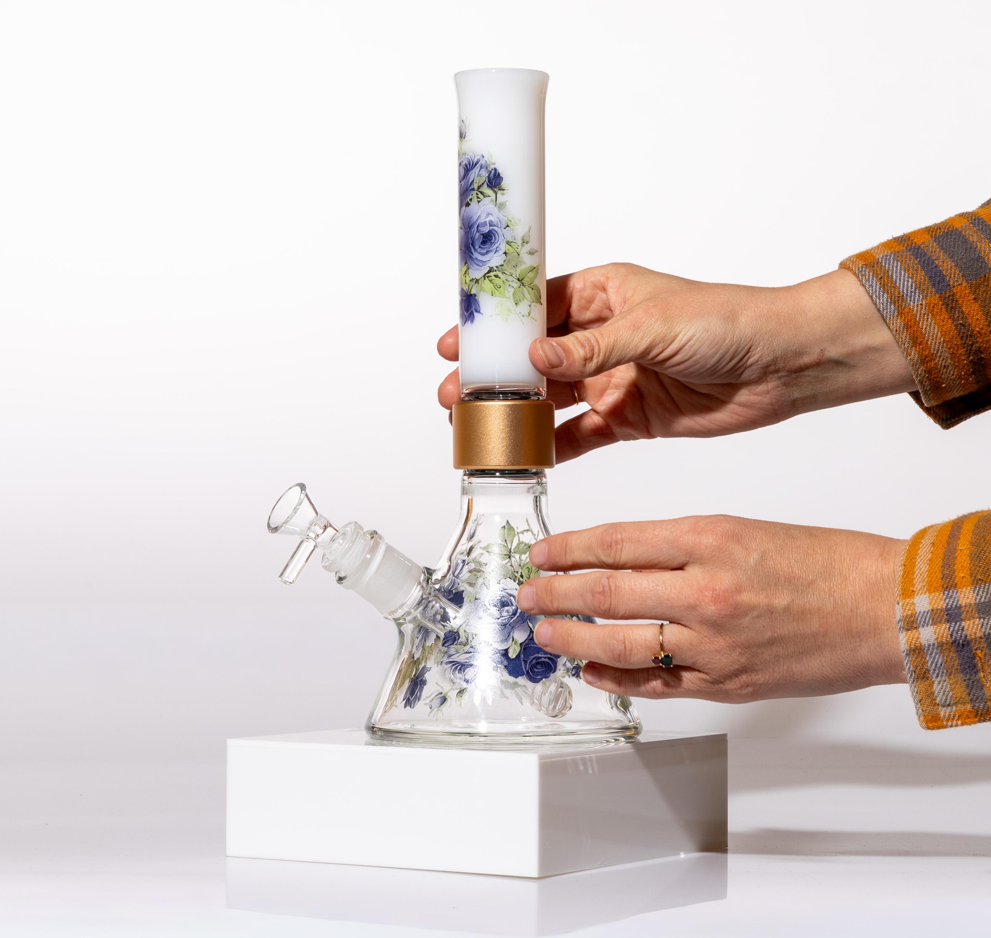 A person holding a compact Prism MINI modular beaker bong with Moonlight Rose decals in their hands to demonstrate its portable travel size and scale.