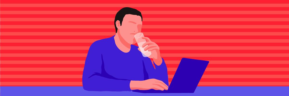 A man sitting on his work desk, drinking a glass of water to stop himself from falling asleep at work.