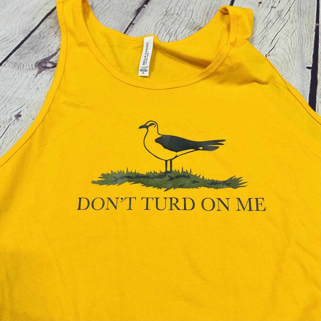 Picture of a gold and yellow men's tank top with a picture of a seagull standing in the grass. Text on the men's tank top says "Don't Turd On Me." Similar to the Gadsden "Dont Tread On Me" Flag