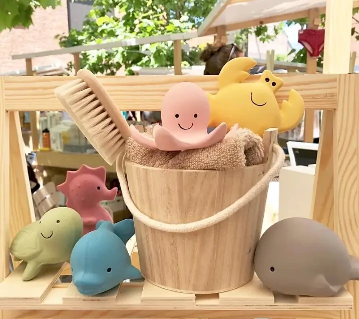 A wooden bucket and brush with several colorful rubber bath toys around it.