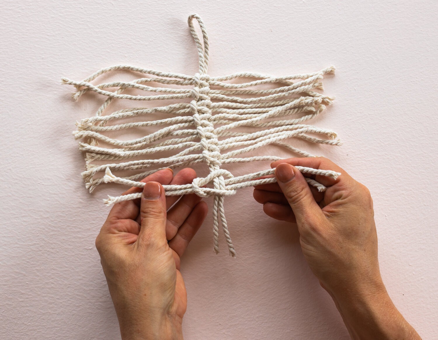A hand ties macrame string together to make macrame leaves.