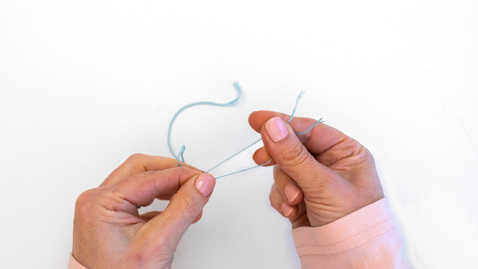 Hands separating a single strand of blue embroidery floss from a longer length of thread.