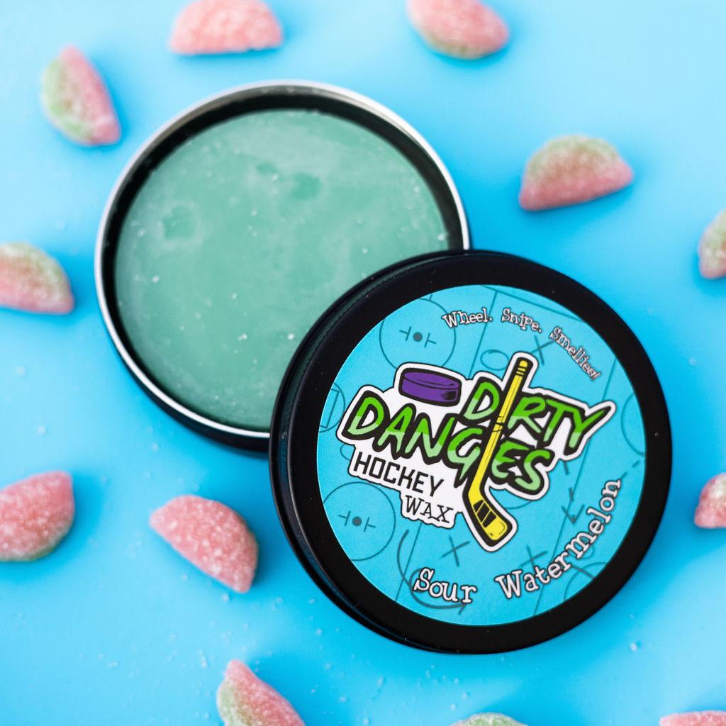 An open tin of dirty dangles sour watermelon hockey stick wax on a blue background with sour watermelon candies