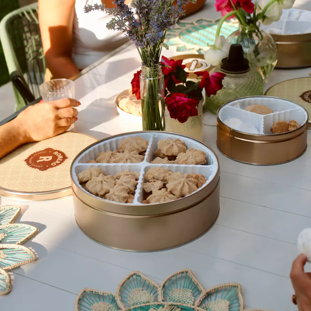 outdoor picnic table set with large open cookie tin and cookies in people's hand