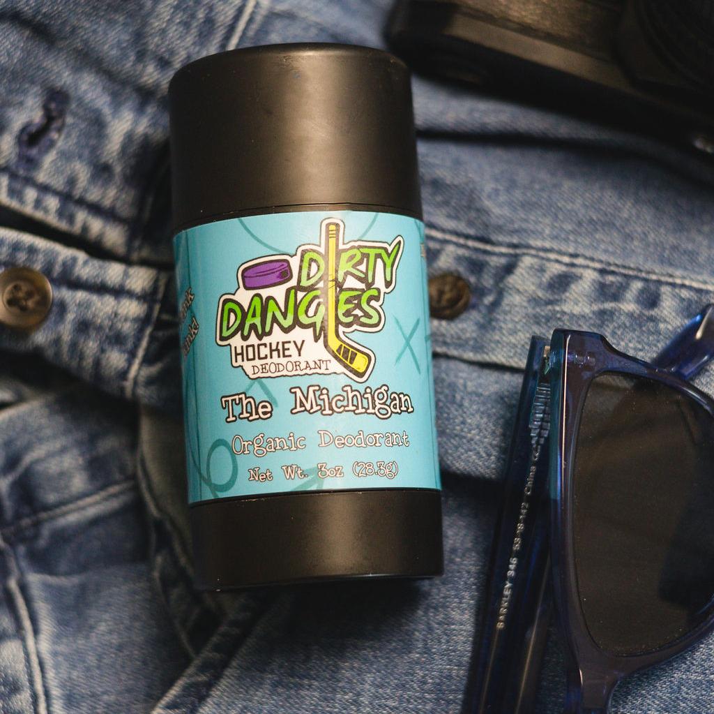 aluminum-free deodorant the michigan scent laying on a pair of jeans with sunglasses and a wallet