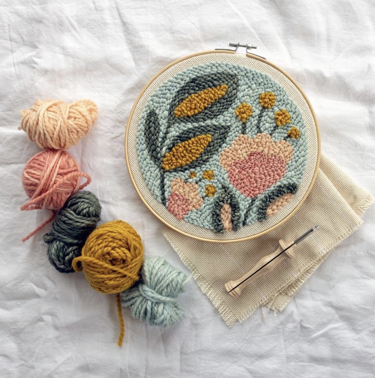 Fabric is pulled tightly in the hoop for the Brilliant Botanicals punch needle pattern. Punch needle supplies surround this project.