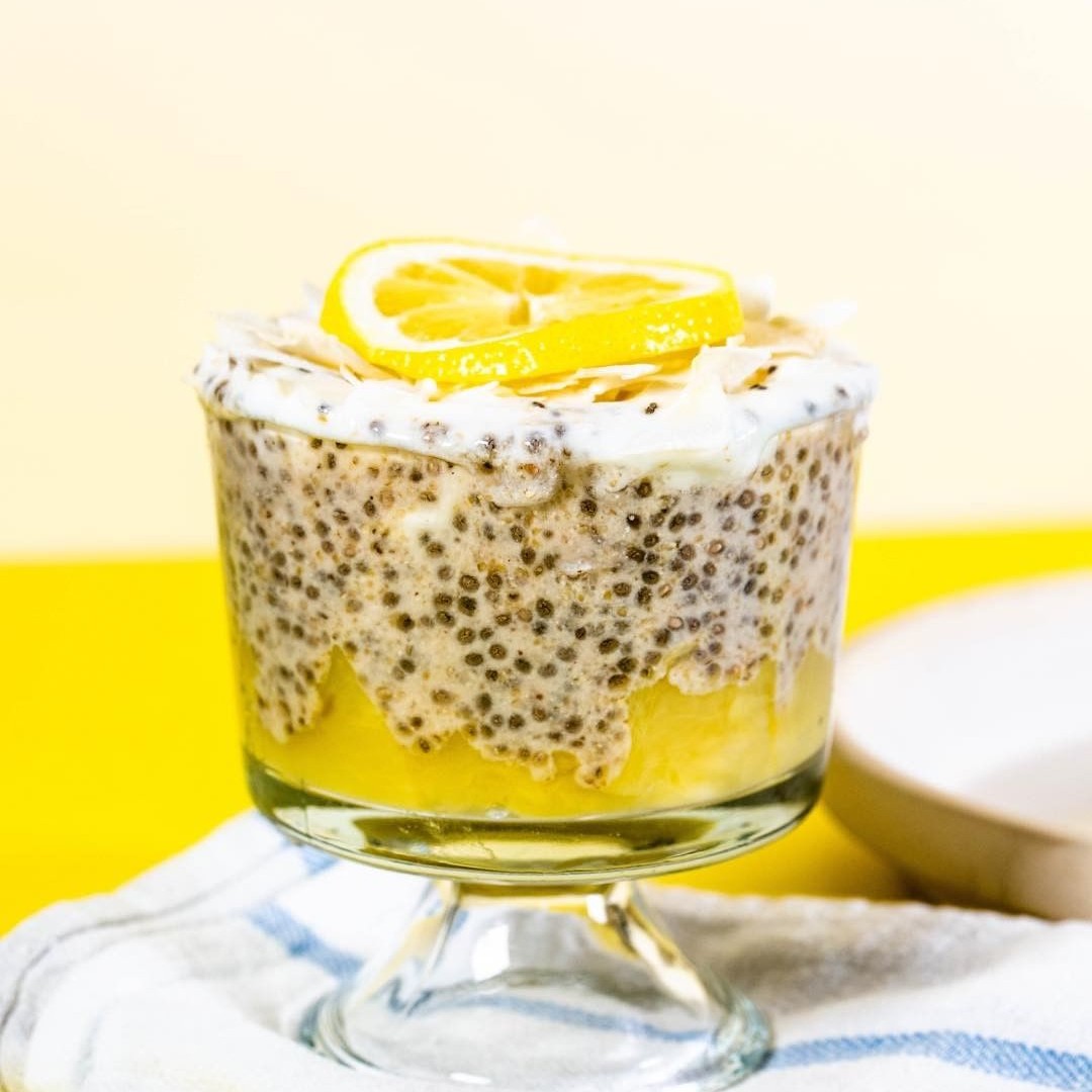 Lemon chia pudding in a glass set on a white cloth and yellow background.