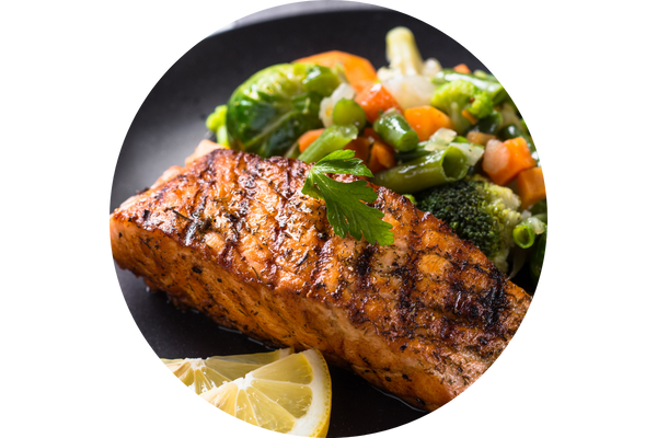 circular image of salmon and with assorted veggies and two lemon slices