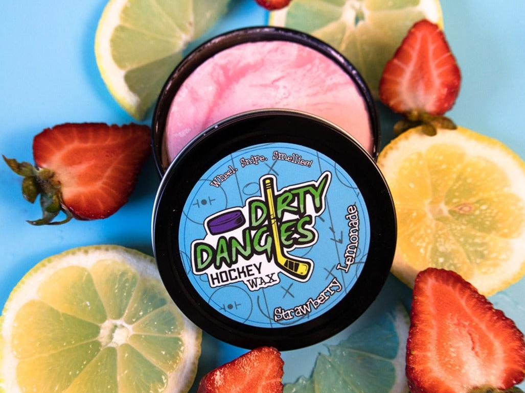A tin of Dirty Dangles Hockey Stick Wax Strawberry Lemonade Scent sits open on a blue background surrounded by Strawberries and lemons