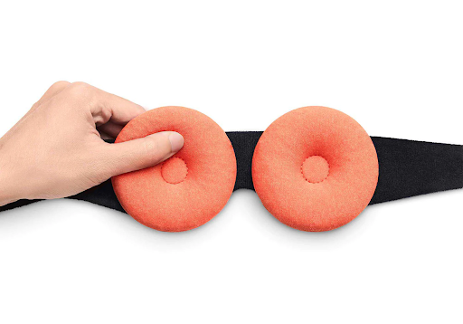 A hand pinching one of two orange heated eye cups of a therapeutic sleep mask.