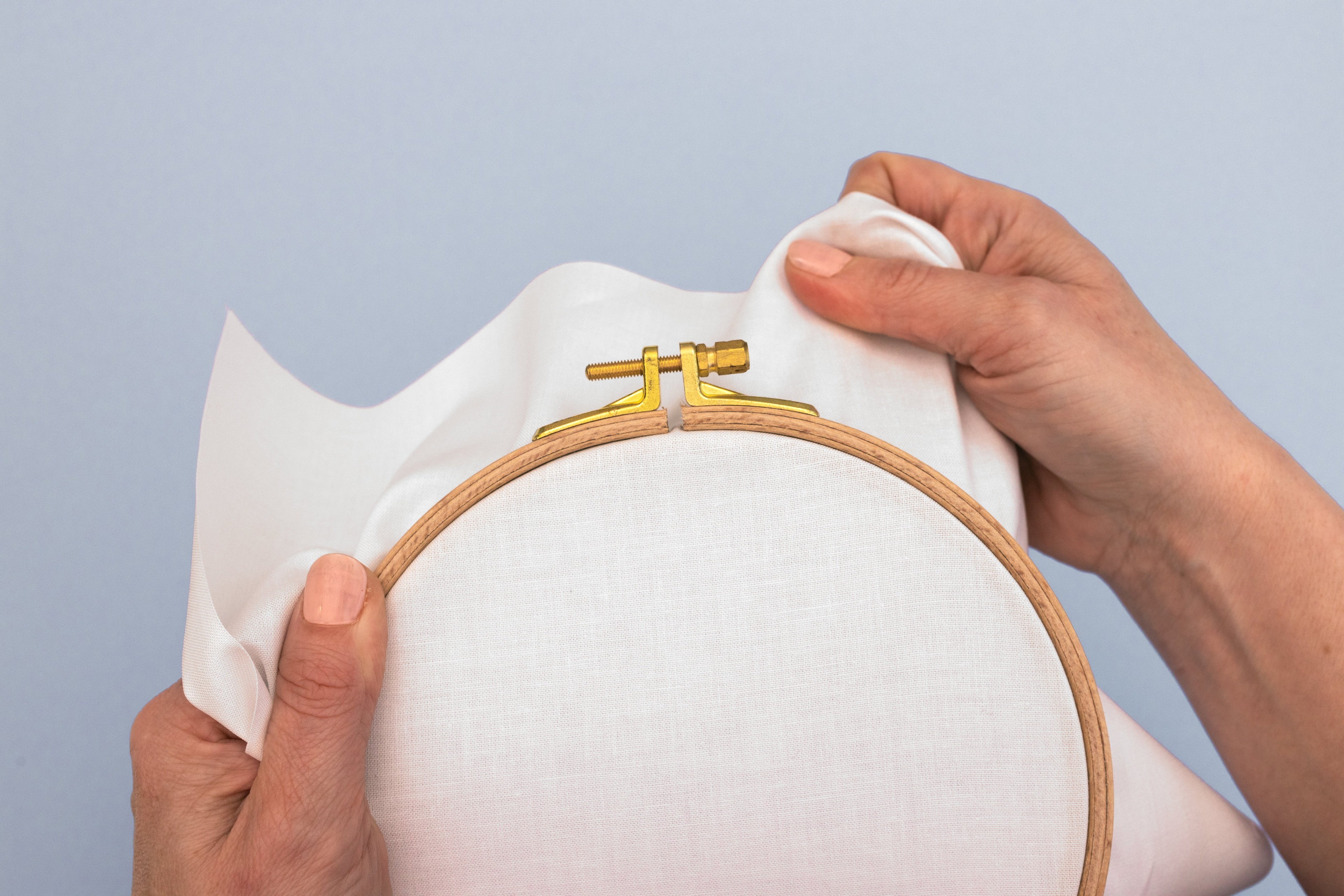 A hand pulls fabric tight in the hoop.