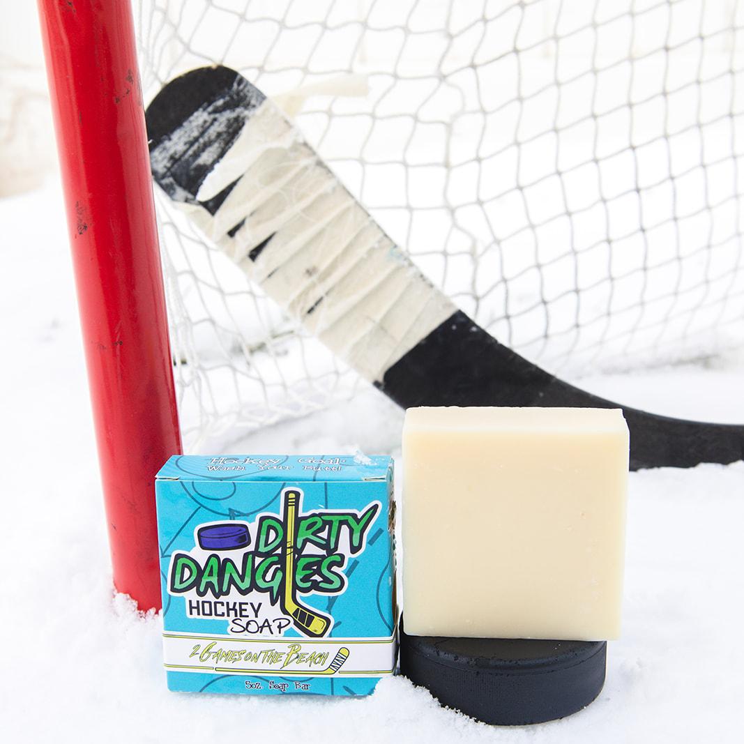 A black soap bar sits in the snow with a hockey goal, hockey puck and a hockey stick. Puck Drop