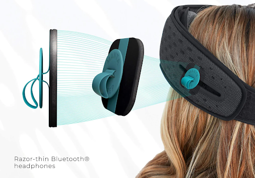 Two speakers with blue tabs and sleep mask that works for light and sound around a head.
