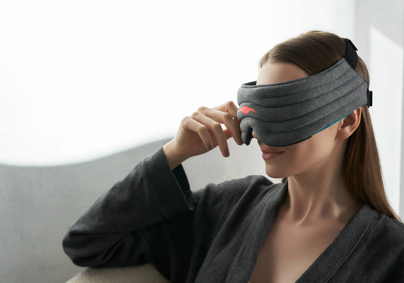A girl holding the edge of a dark gray weighted sleep mask that she is wearing.