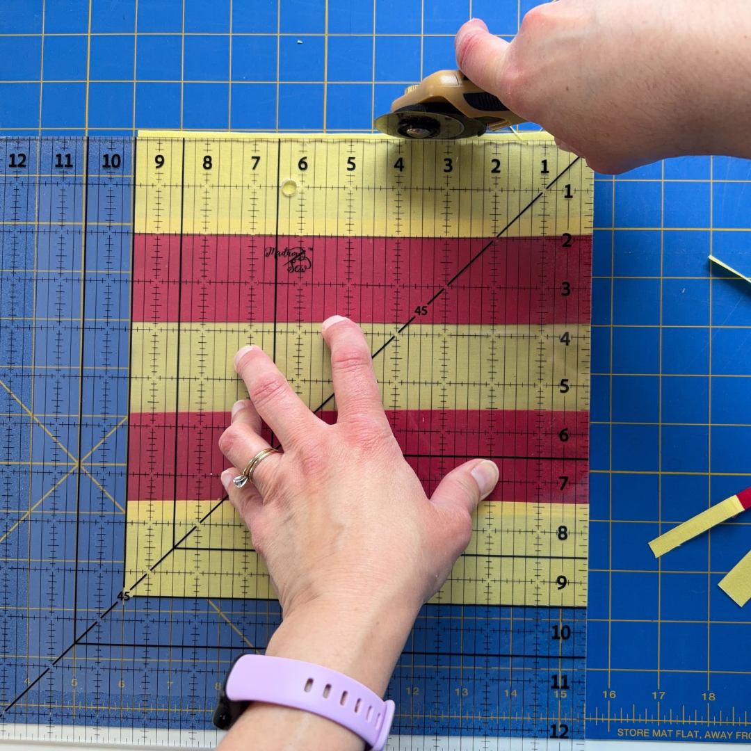 Cutting along the top edge of the Madam Sew 12.5” Square Up ruler while the opposite block edge is aligned on the 9.5” line.