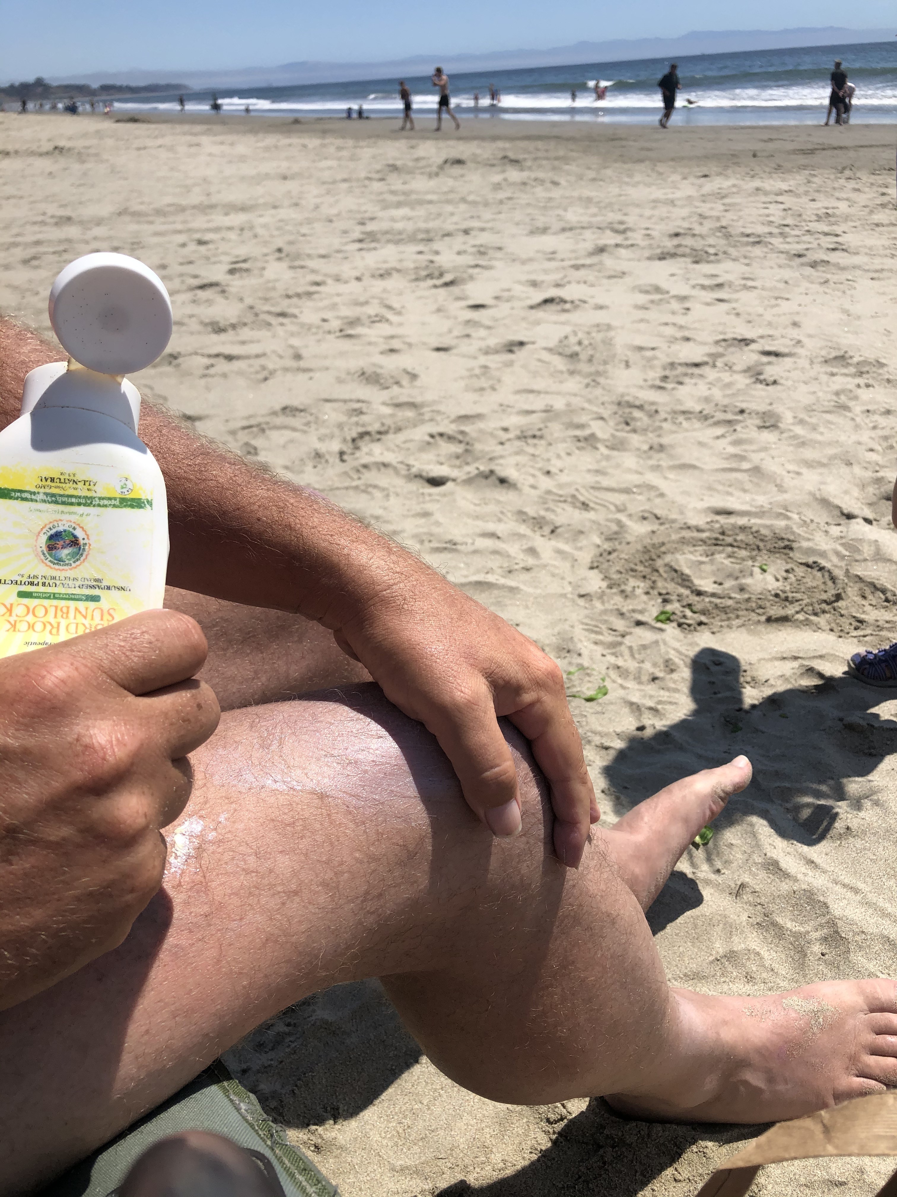 Applying reef safe sunscreen to a man's legs at the beach