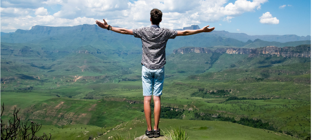 Man standing on summit of a hill with arms raised to his sides