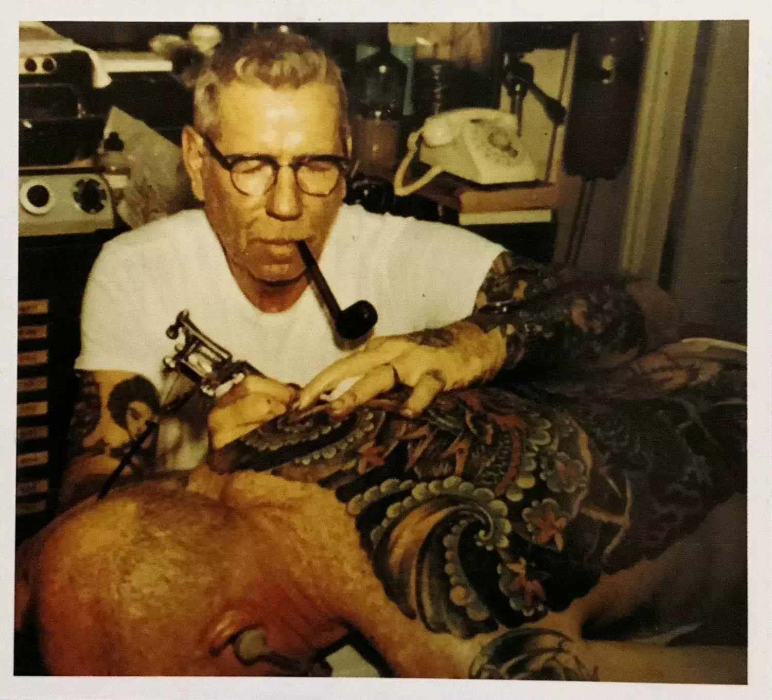 Historical photo of legendary tattoo artist Sailor Jerry applying an American Traditional tattoo to a marine, showcasing the origins of classic tattoo flash and enduring style in naval ports and military culture.