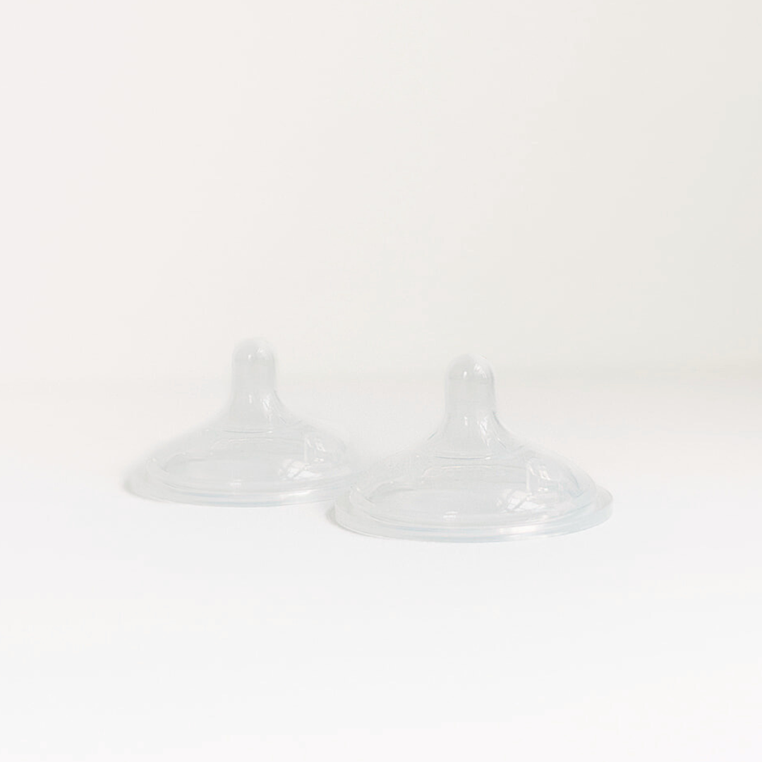 Two transparent silicone baby bottle nipples on a white surface
