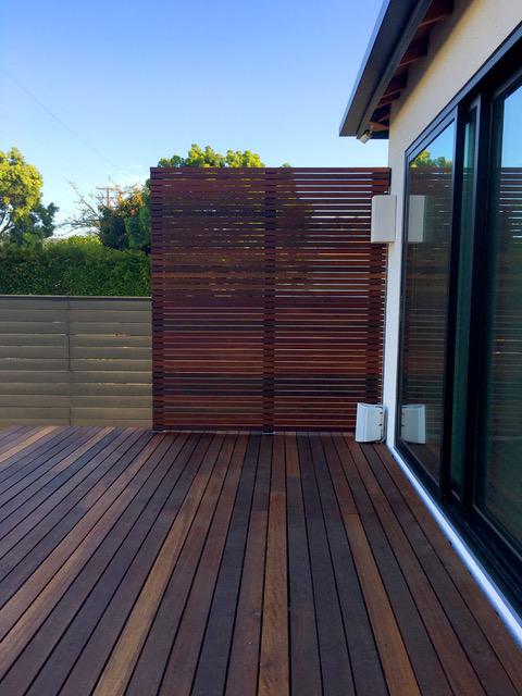 Modern dark chestnut privacy wall and deck with blue skies and foliage in the background