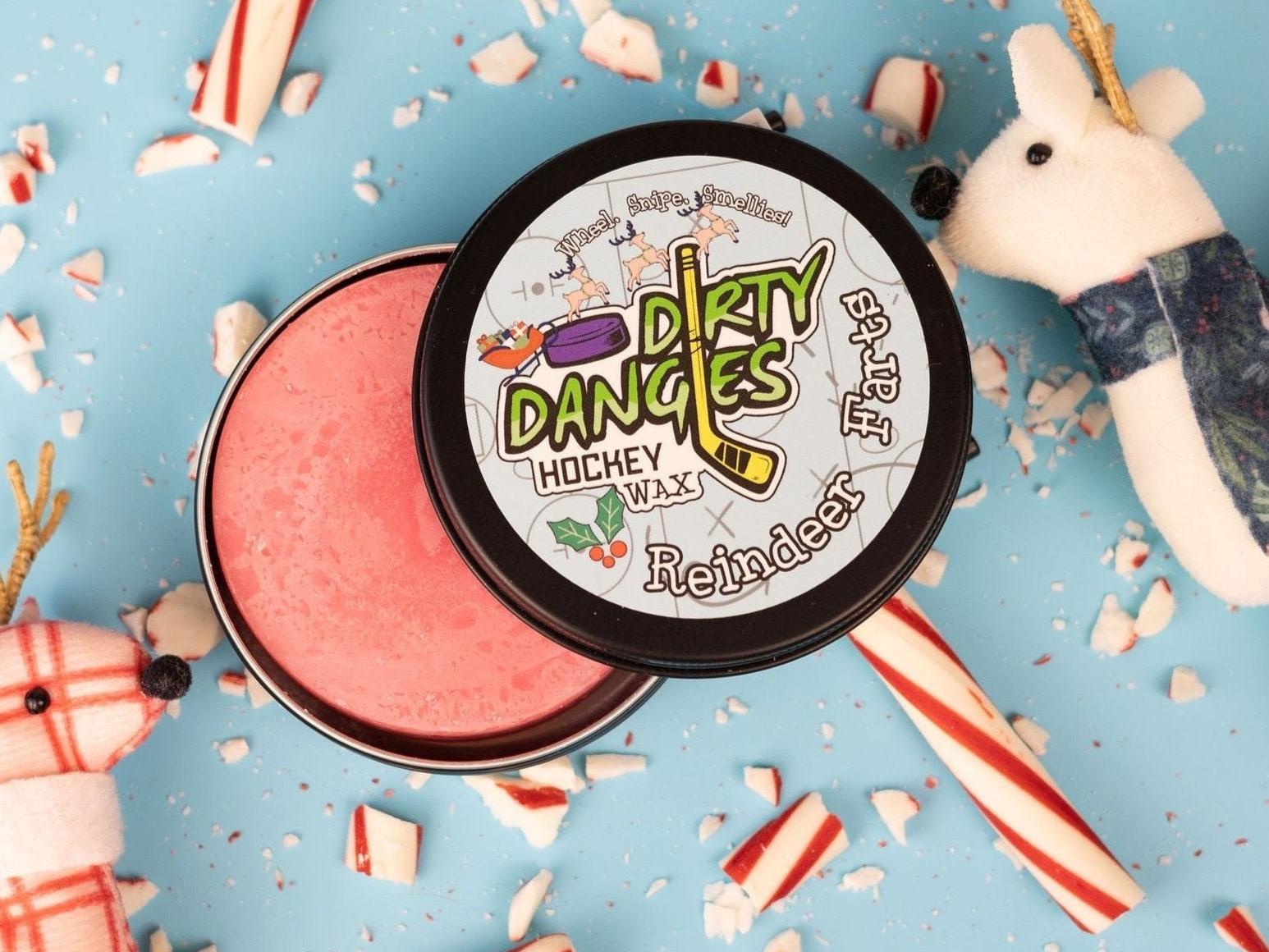 A tin of dirty dangles reindeer farts holiday hockey stick wax on a blue background with candy canes and reindeer