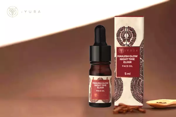 a beautiful photo of Manjish Glow Elixir - iYURA's bestselling night oil - accompanied by its beautifully illustrated, protective cylinder packaging