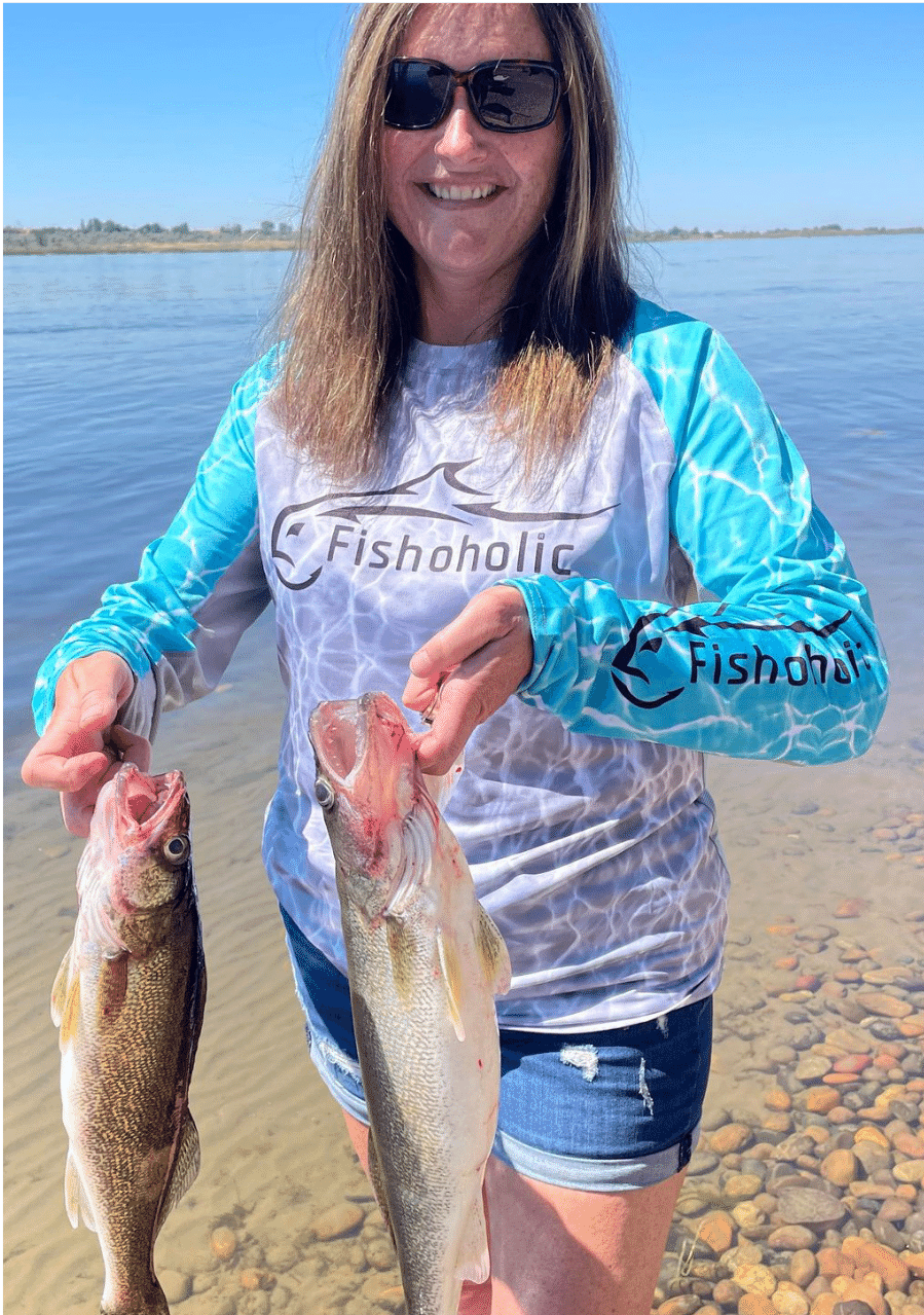 Woman holding up two fish wearing Fishoholic fishing shirt on a beach