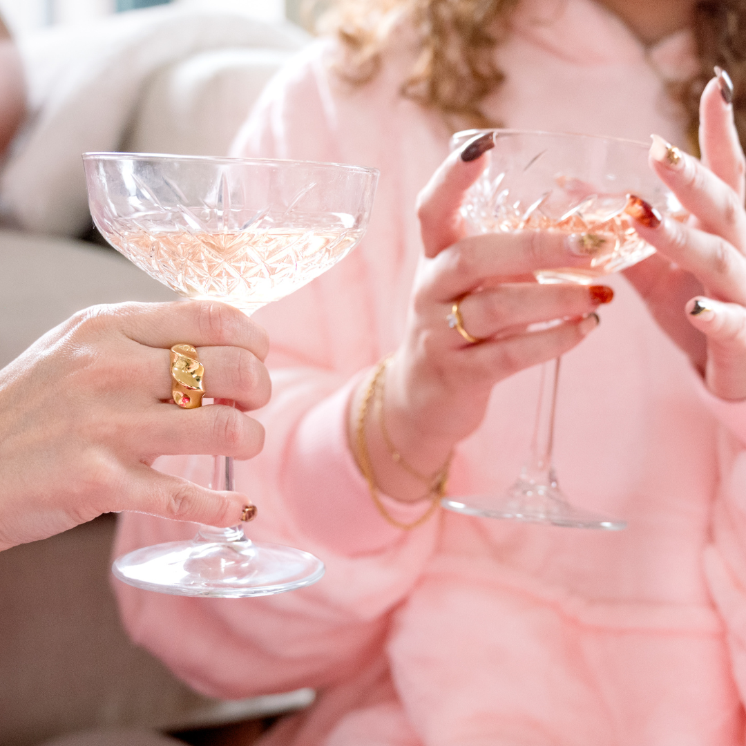 Two people holding glasses wearing gold rings and bracelets