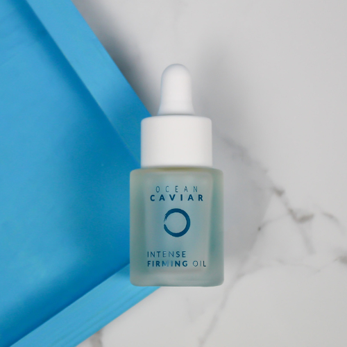Ocean Caviar Firming Oil laying on a blue corner and white marble background
