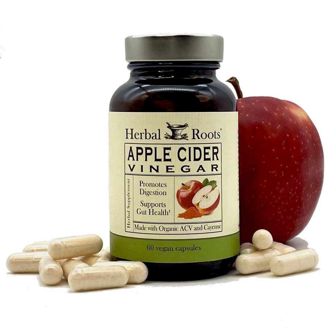 Bottle of Herbal Roots Apple Cider Vinegar with capsules on either side of bottle and a whole red apple peeking out on the right side from behind the bottle