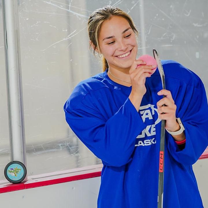 Girls hockey player applying Dirty Dangles hockey stick wax to her stick at the rink.