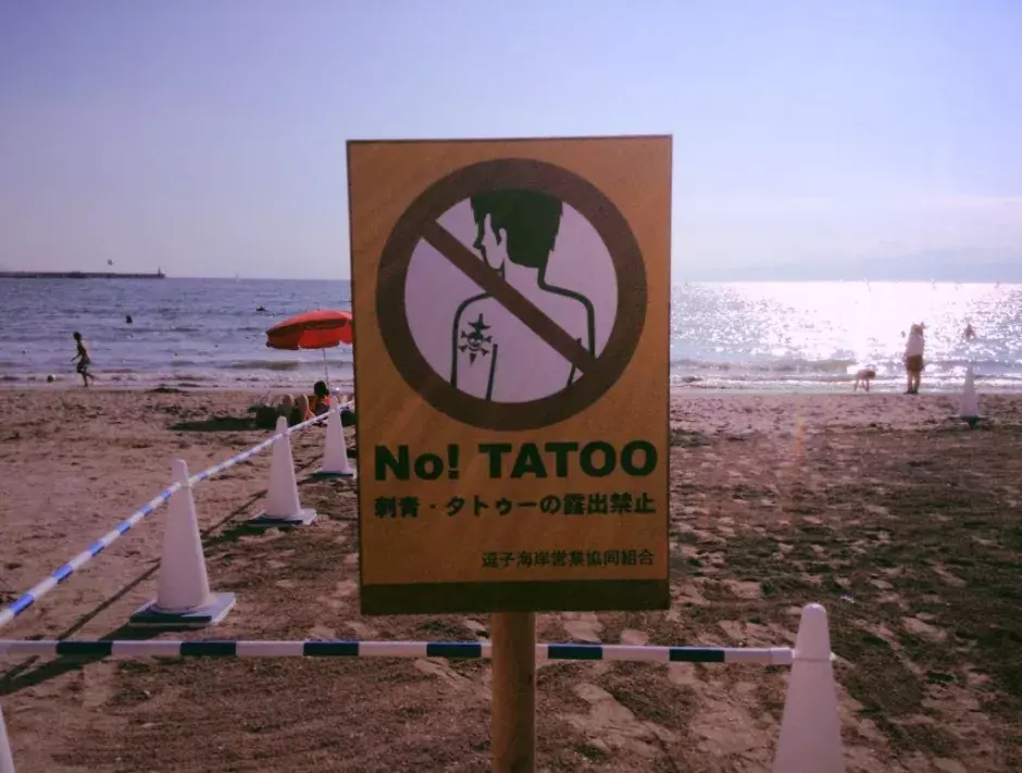 Photo of a Japanese sign banning tattoos on a beach, symbolizing the historical social stigma and taboo against permanent self-expression, mirroring the cultural journey of functional glass smokeware and cannabis culture.