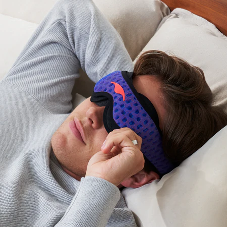 Man touching the edge of a blue sleep mask — a photo for an article on how electronics affect sleep.