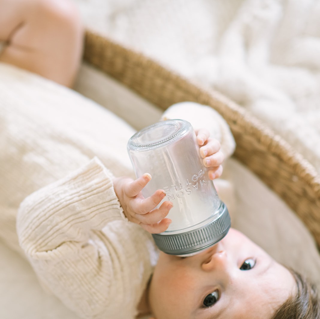 baby laying in basket drinking from anti-colic glass baby bottle