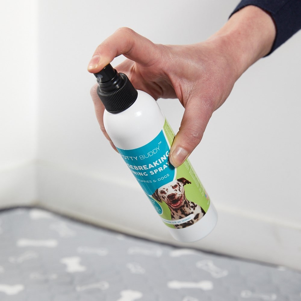 A hand spraying the Potty Buddy Housebreaking Training Spray on a reusable pee pad