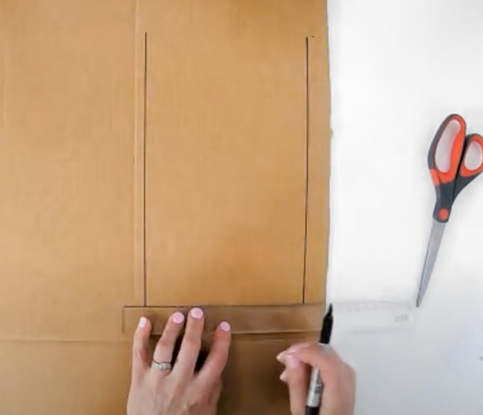 This is an image of hands drawing on a cardboard sheet with a ruler and vivd.