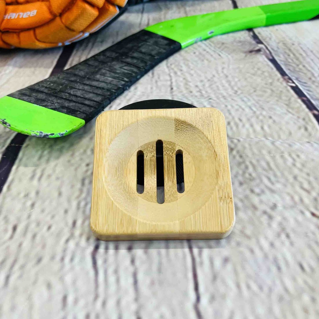 a bamboo soap dish sits on a wood background with a hockey stick and hockey gloves